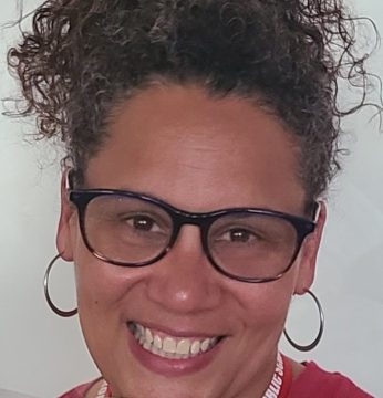 A woman wearing glasses and a red shirt is smiling.