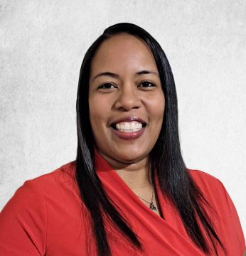 A woman with long, straight black hair is smiling and wearing a red top against a light gray background.